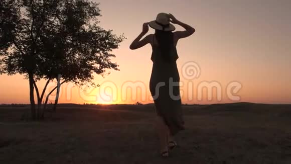 一位戴着帽子和长裙的年轻女子在田野上朝夕阳走来的剪影视频的预览图