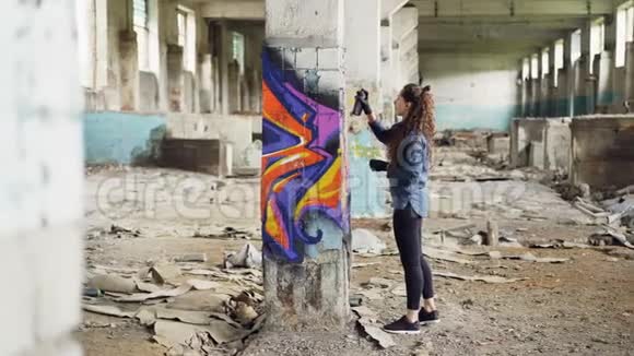 漂亮的女孩涂鸦艺术家用抽象的图片在空荡荡的工业大楼里装饰旧的损坏的柱子视频的预览图