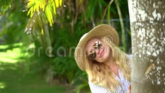 美丽的旅行者女人带着帽子在棕榈树后面微笑阳光概念旅行度假视频的预览图