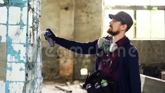 英俊的城市艺术家正忙着在废弃的房子里用耳塞油漆装饰脏损坏的柱子创造视频的预览图