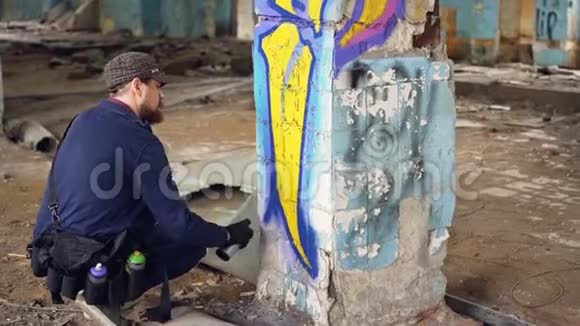 现代涂鸦画家蹲在旧废弃建筑的柱子附近用喷漆涂鸦视频的预览图