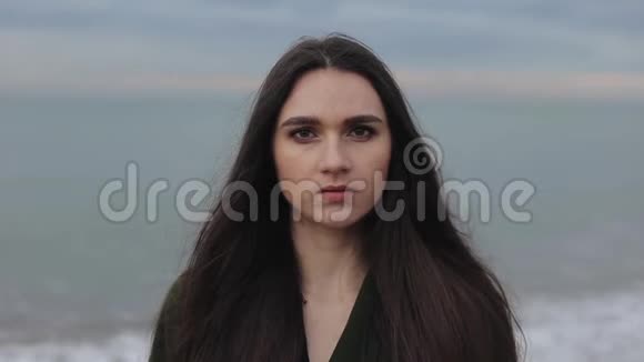 一个美丽的独立女人站在海滩上看着相机特写肖像模糊的背景视频的预览图