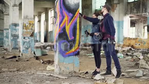 专业的涂鸦画家正在教漂亮的女孩在被遗弃的时候一起工作时使用喷漆视频的预览图