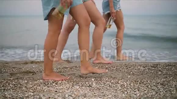 孤立地观看三双纤细的女性腿手里拿着玻璃瓶踩在海边视频的预览图