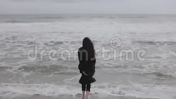一个穿暖和衣服的光脚漂亮的女孩在寒冷的一天朝大海跑去害怕冷水跑起来视频的预览图
