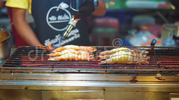 厨师手里拿着烧烤炉在夜市的烤架上做新鲜的大虾视频的预览图