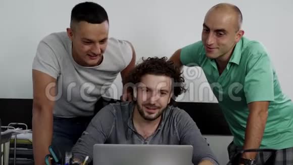 三个年轻可爱的雄性正在看手提电脑并快乐地笑在一起视频的预览图