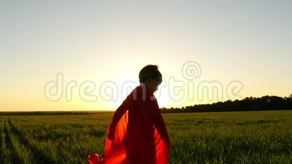 穿着超级英雄服装穿着红色斗篷的男孩在一片绿色草坪上奔跑背景是一场日落模拟视频的预览图