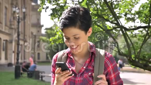可爱的快乐女人留着黑色短发打着电话对着镜头微笑站在大学附近的街道上视频的预览图