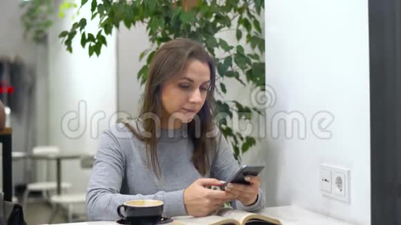美丽的女人把时间花在咖啡馆里看书打电话喝咖啡视频的预览图
