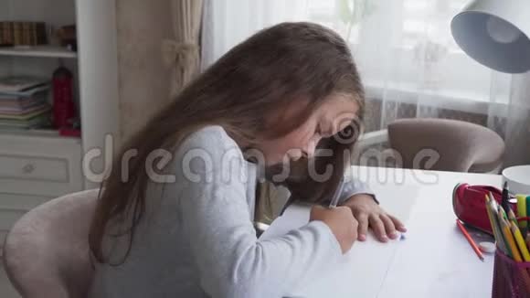 可爱的小女孩坐在桌子旁在家做作业视频的预览图