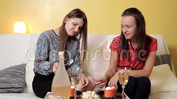 两个年轻女孩坐在家里的沙发上喝着葡萄酒吃着蛋糕聊天友谊甜蜜视频的预览图