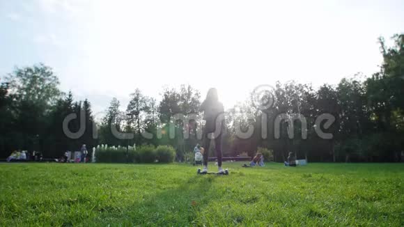 一个年轻的女孩有一个漂亮的身材骑着陀螺在公园的草地上阳光灿烂视频的预览图