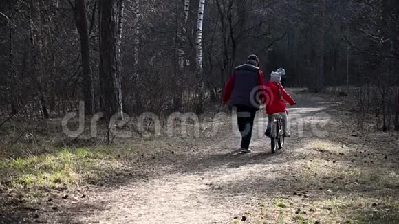 爷爷带着一个孩子孙女在山林公园里骑自行车森林小径视频的预览图
