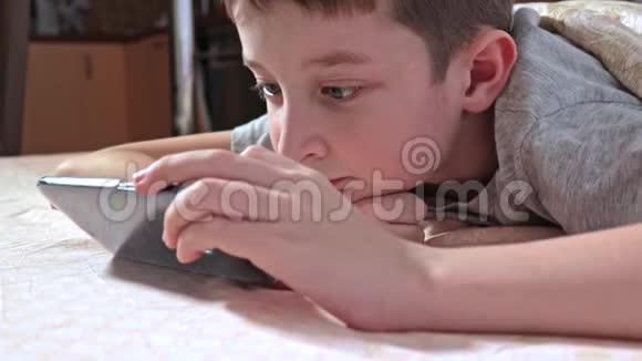 一个男孩躺在家里的床上在智能手机上放松和观看视频视频的预览图