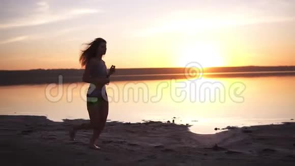 美丽的跑步女子跑过日落年轻女子沿着海边慢跑健康的生活方式观念慢动作视频的预览图