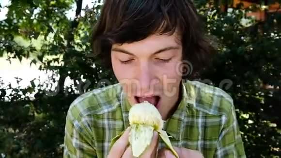 一个年轻人在一个夏季公园的特写镜头中吃一个成熟的无花果的肖像动作缓慢视频的预览图