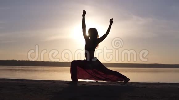 一个苗条的女孩做战士的剪影在日落时做瑜伽姿势海滨视频的预览图