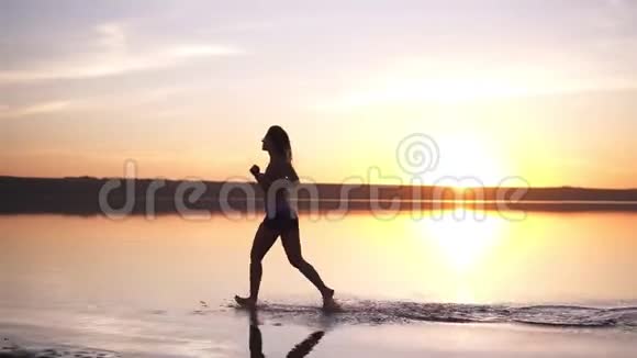 有长发的苗条女人在户外跑步在水边慢跑海边太阳照耀着背景视频的预览图
