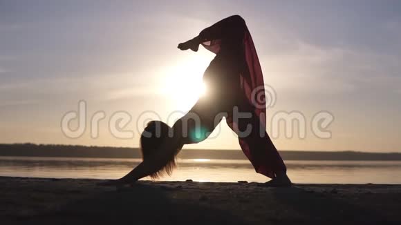 一名白种人妇女在户外练习瑜伽在日落和大海上孤立的剪影视频的预览图