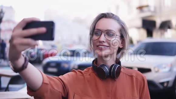 穿着橙色衬衫和太阳镜的开朗迷人的女性在智能手机摄像头上自拍摆姿势站立视频的预览图