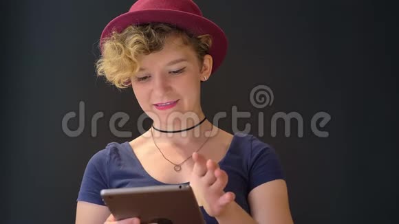 迷人的幸福女人一头卷曲的金发在平板电脑上打字在镜头前微笑被隔离在黑色背景上视频的预览图