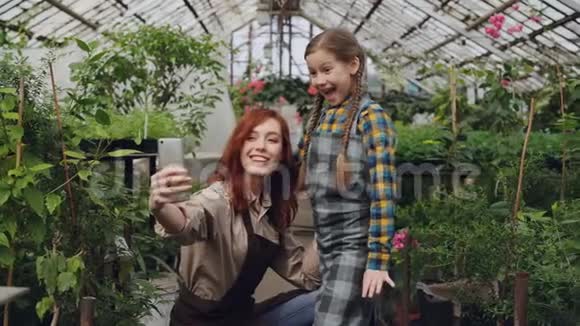 可爱的母亲和顽皮的女儿正在温室里自拍摆姿势打手势做有趣的脸家庭视频的预览图