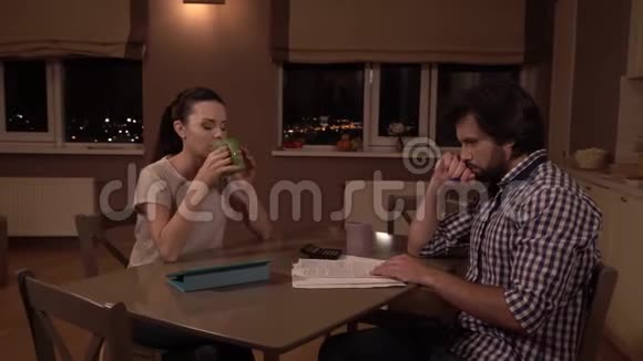心烦意乱的男人和女人坐在桌子上他们在思考女孩从杯子里喝酒看着丈夫他看报纸视频的预览图