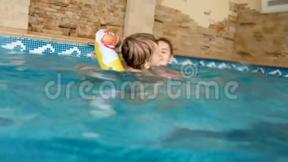 4k视频快乐的年轻妈妈教她的小儿子在室内游泳池游泳视频的预览图