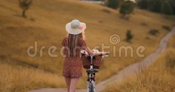 微笑着快乐的女孩穿着连衣裙和帽子骑着复古自行车在公园里看着相机视频的预览图