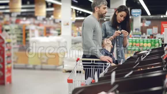 快乐的小家庭在超市购物妈妈在检查集装箱里的食物爸爸在和他快乐的聊天视频的预览图
