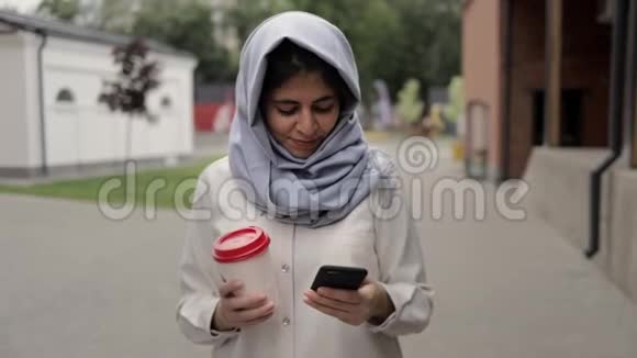 戴头巾的年轻女子喝着咖啡看着手机视频的预览图