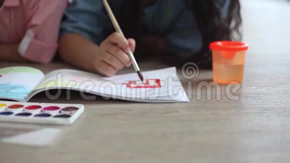 一个小男孩和一个小女孩躺在地板上用画册上的颜料作画特写高清视频的预览图