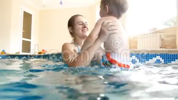 年轻的妈妈抱着小儿子在家里的游泳池里旋转的4k视频视频的预览图