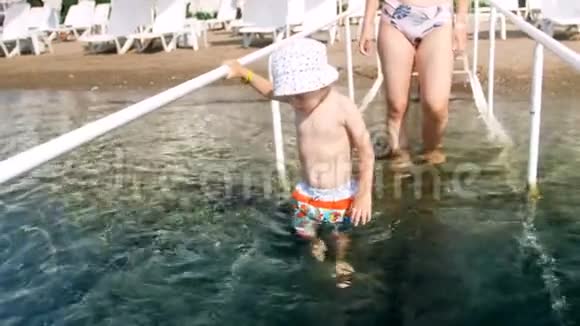 4k视频带着母亲在海水中漫步的带栏杆的儿童微笑视频视频的预览图