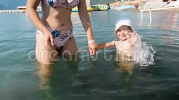 4k视频快乐欢笑幼儿男孩手牵妈妈走在海里视频的预览图