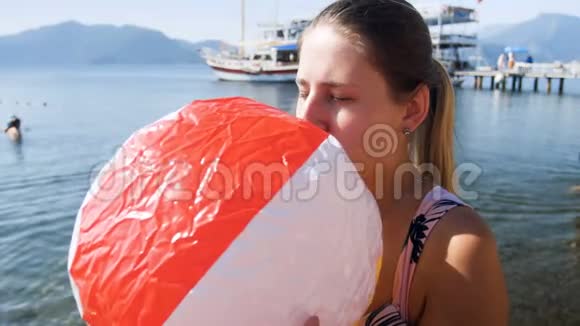 4k视频年轻女子在海上吹着充气的彩色沙滩球视频的预览图