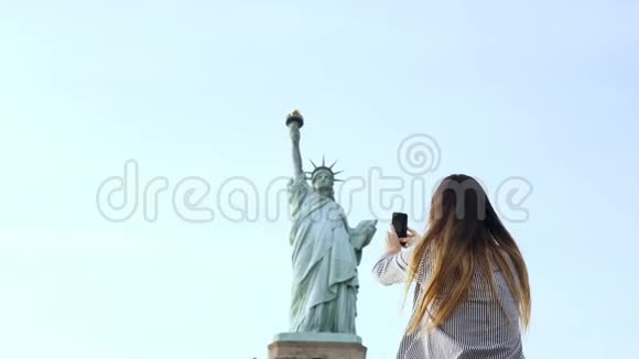 美丽微笑的欧洲旅游妇女在纽约市拍摄自由女神像的智能手机照片视频的预览图