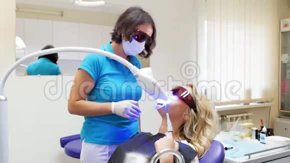牙科医生在牙齿美白过程中与躺在牙科椅上的病人谈话的4k录像视频的预览图