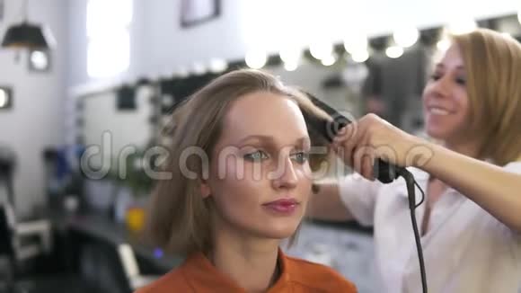 漂亮的白种人女孩在美容院化妆理发师用熨斗烫直头发模糊的视频的预览图