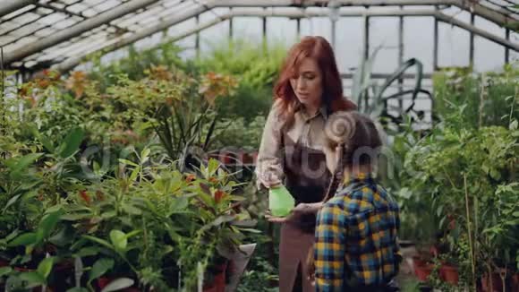 快乐的女园丁洒水在植物上和她可爱的小女儿一起玩生长的花朵视频的预览图