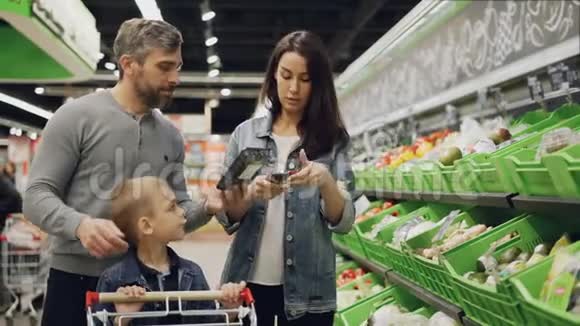帅哥他迷人的妻子和可爱的孩子正在超市的托盘里挑选蔬菜视频的预览图