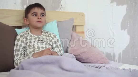生病的小男孩坐在床上咳嗽用毯子盖着自己视频的预览图