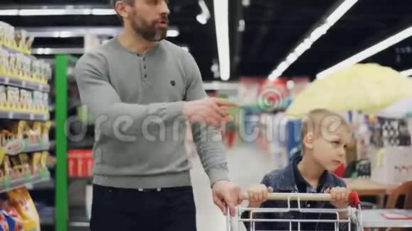 快乐的男人正在和他快乐的孩子一起购物他们在超市里用购物车走来走去视频的预览图