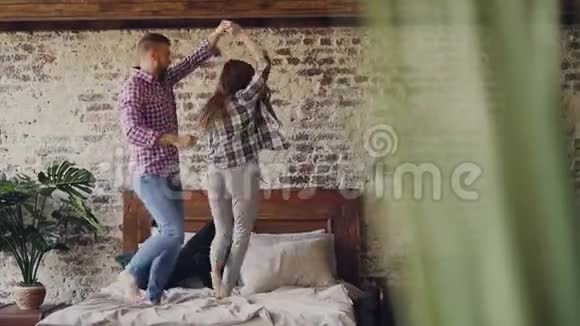 有趣的年轻夫妇正在床上跳舞在旅馆里玩得很开心笑得很开心快乐的人度假现代生活方式视频的预览图