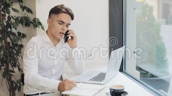 中镜头集中年轻商人在咖啡休息时打电话时在笔记本上记笔记视频的预览图