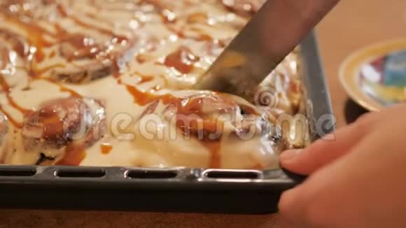 女人或男人用一把特殊的刀从盘子里切出一个新鲜的热肉桂包上面铺着白色的奶油焦糖视频的预览图