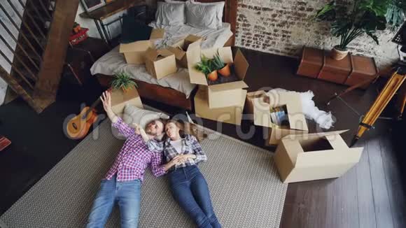 在新房子的卧室地板上躺着有吸引力的夫妻和交谈的顶部景色年轻家庭视频的预览图