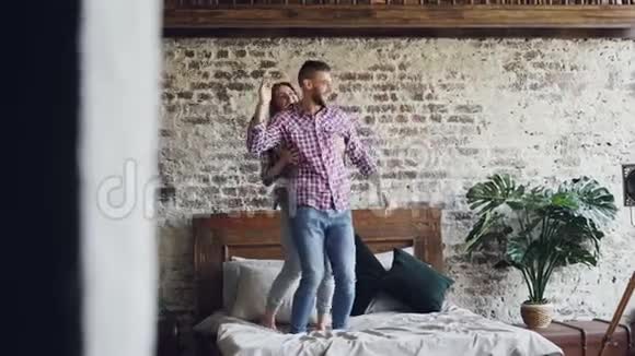 有趣的年轻夫妇正在床上跳舞在阁楼风格的卧室里玩得很开心笑着快乐的人现代的生活方式视频的预览图