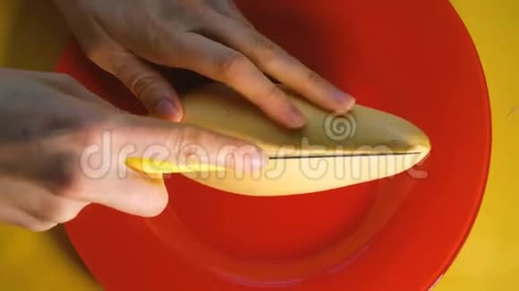 女性手在黄色背景的红色盘子上用刀切下一个成熟的泰国芒果俯视图视频的预览图